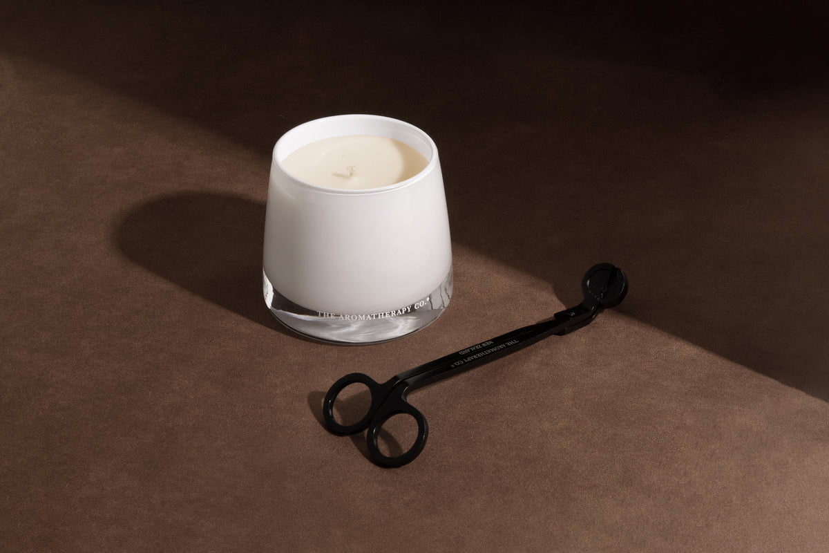 Lit Therapy candle in frosted white glass beside a black wick trimmer on a warm brown surface
