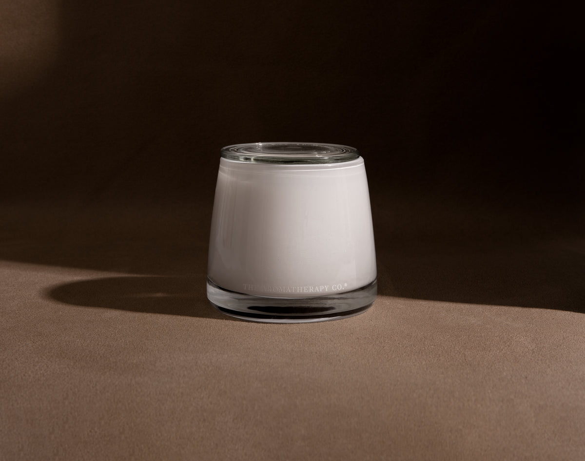 Therapy candle in frosted white glass on a brown surface against a dark backdrop