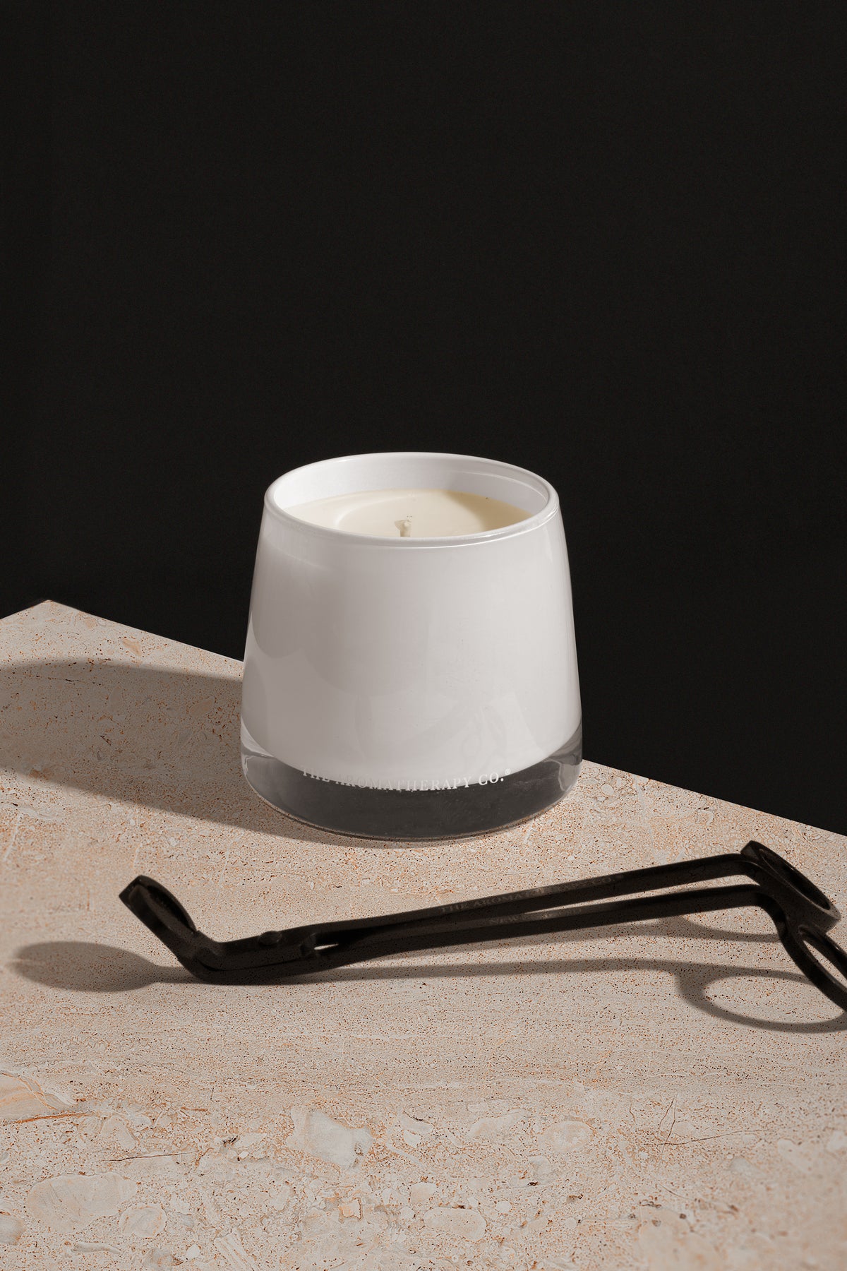 Therapy candle on a pale stone block with a wick trimmer against a dark wall