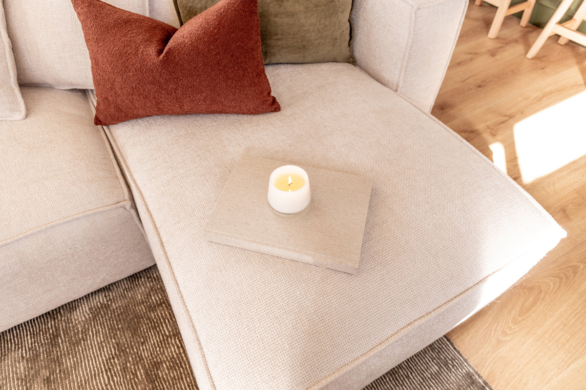 Lit Therapy candle on a coffee table beside a rust cushion