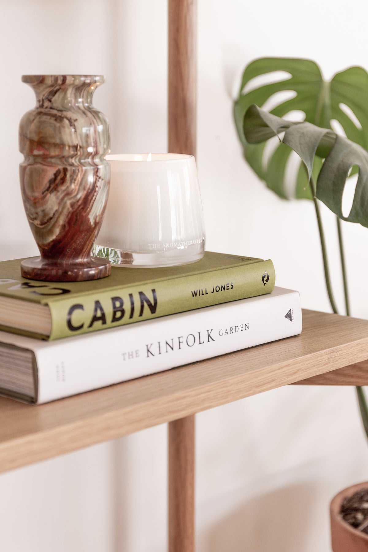Therapy candle on an oak shelf with a stone vase, stacked books and a monstera leaf