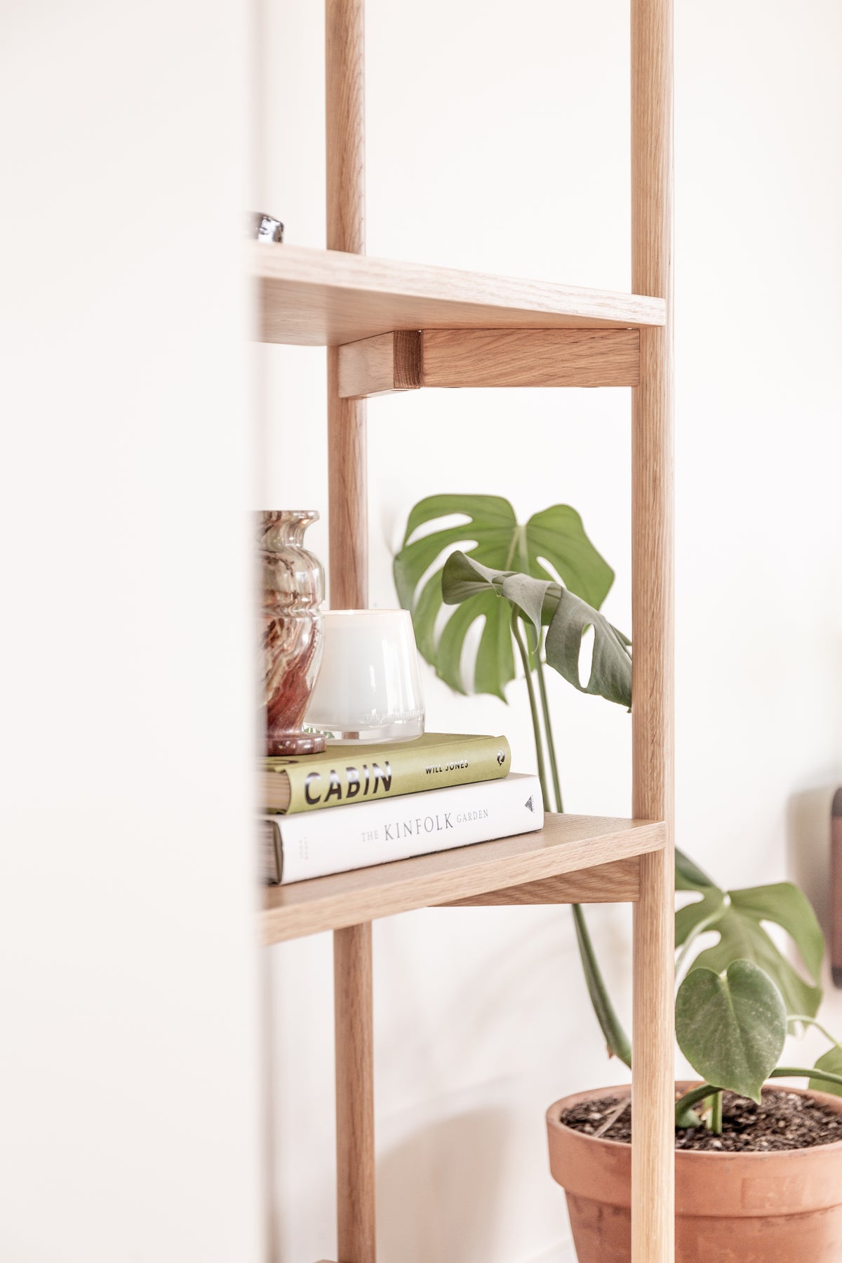 Oak shelving with a Therapy candle, books and a potted plant in a bright room