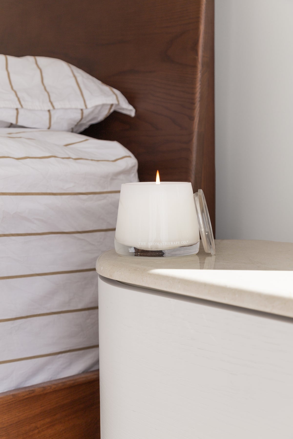 Therapy candle on a bedside table next to striped bedding