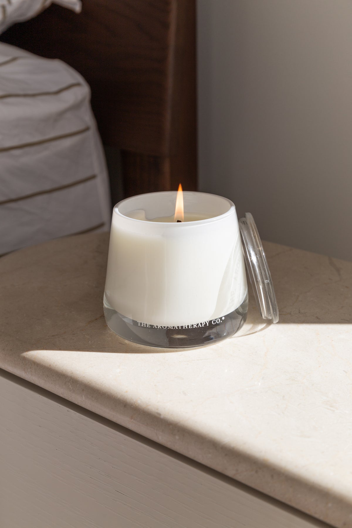 Therapy candle on a white bedside table beside a striped bed