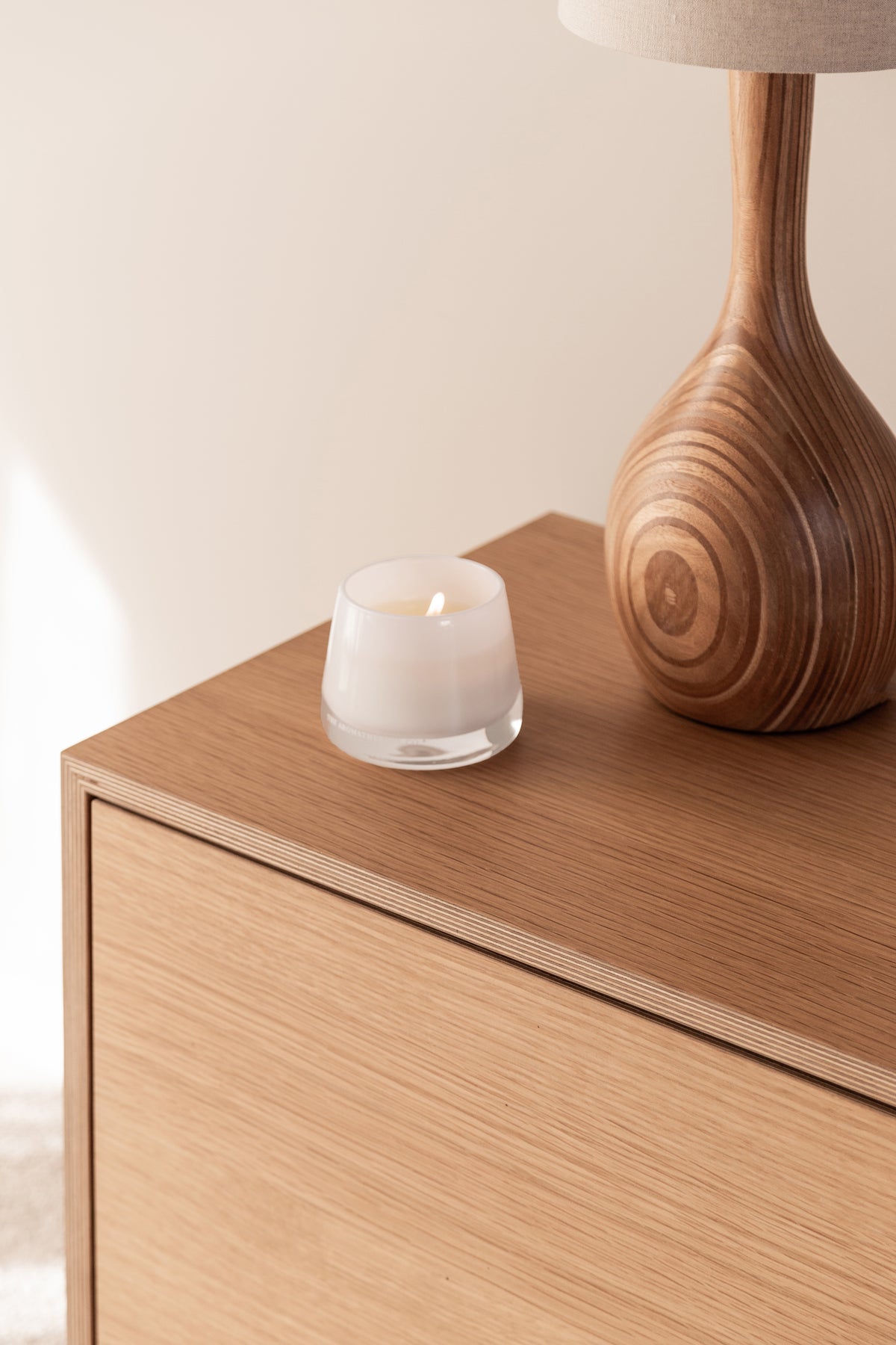 Therapy candle on a timber bedside cabinet beside a wooden lamp base