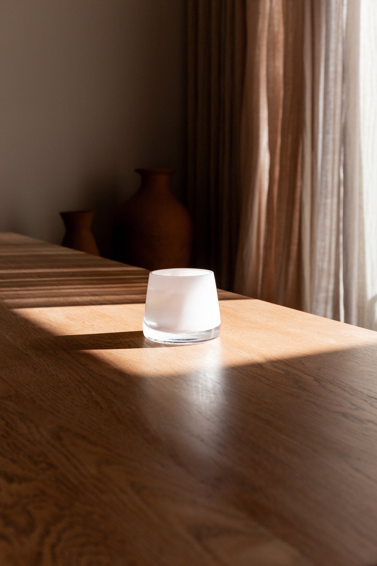 Therapy candle on a timber table with terracotta vases behind