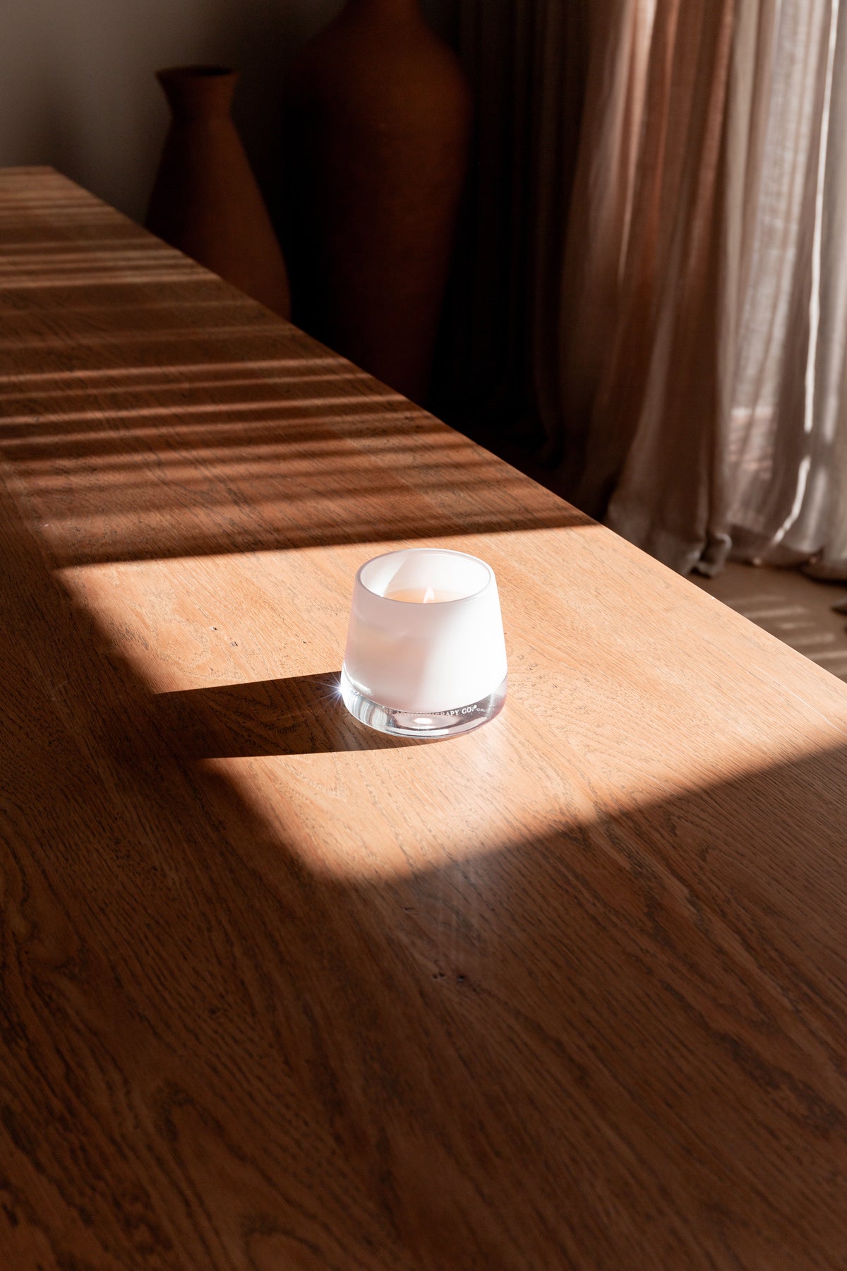 Therapy candle on a timber sideboard in striped afternoon light