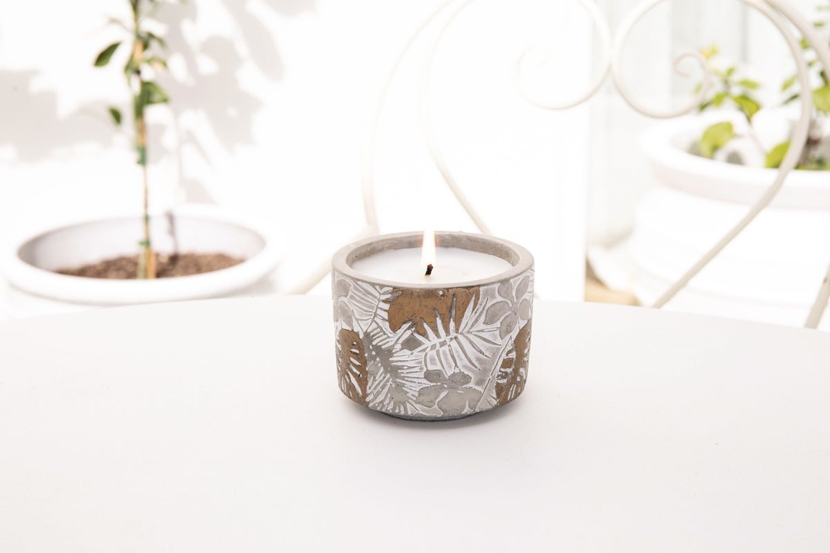 Lit candle centred on a white round table between potted seedlings and a curved white chair