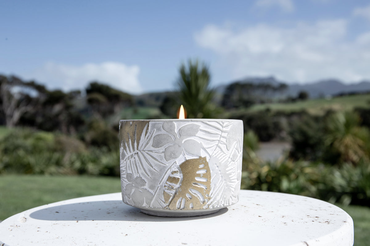 Lit candle on a white concrete plinth outdoors with green hills and blue sky