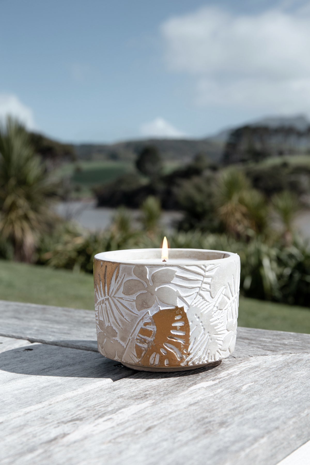 Portrait shot of the lit candle on a weathered timber deck with native bush and hills behind