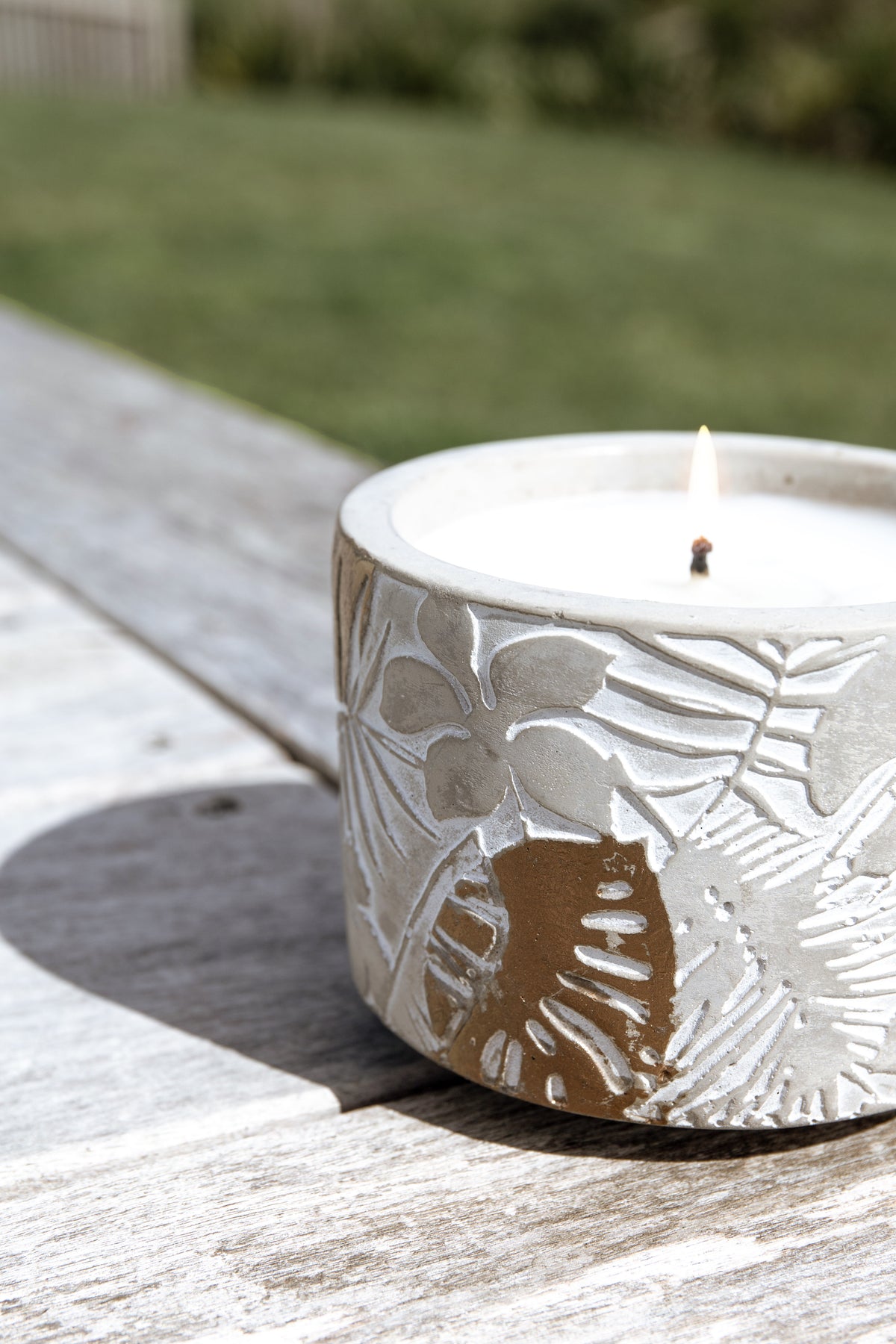 Lit citronella candle close up on grey weathered timber with a green lawn behind