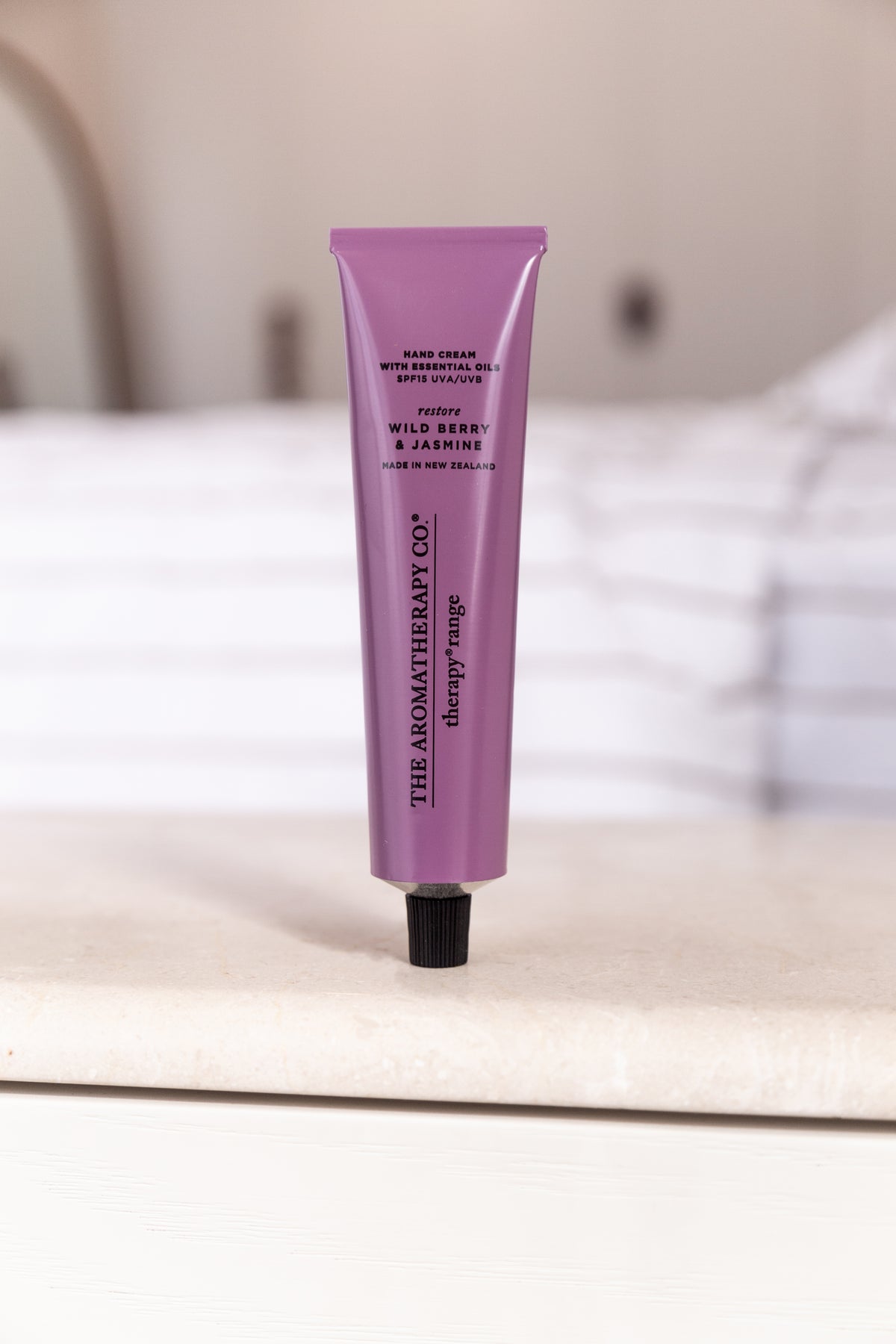 Wild Berry & Jasmine hand cream upright on a stone ledge with a striped linen bed behind