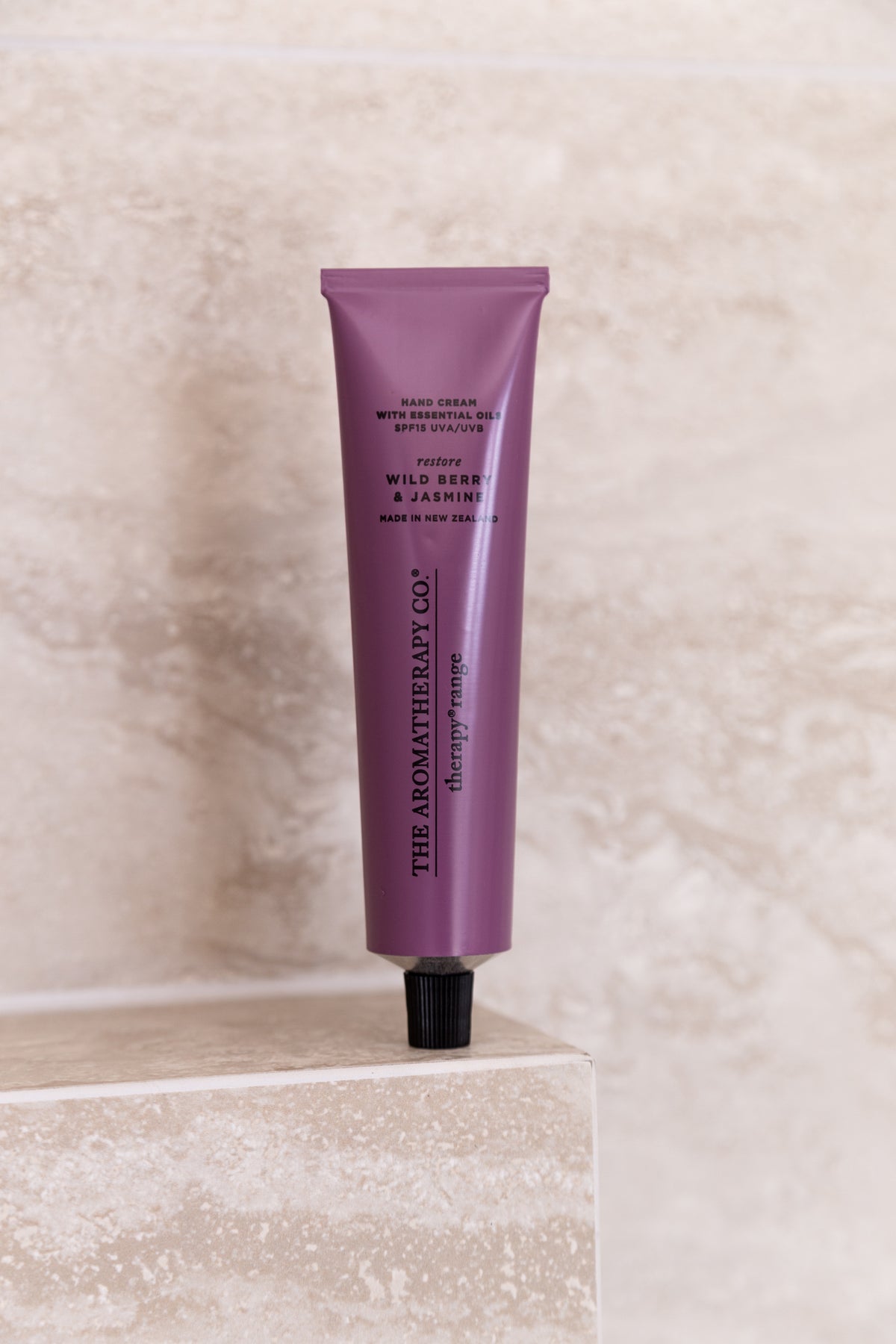 Wild Berry & Jasmine hand cream standing upright on a travertine block against a stone wall