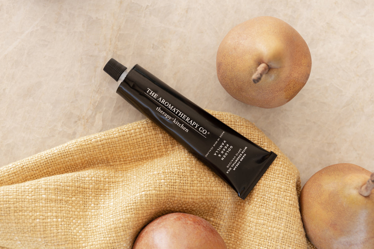 Golden Pear & Vanilla hand cream tube on a mustard linen napkin with whole pears on pale stone