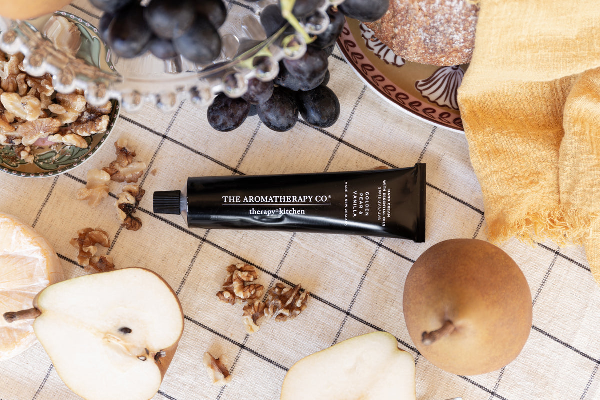 Hand cream tube centred on a check cloth among walnuts, grapes and halved pears, seen from above