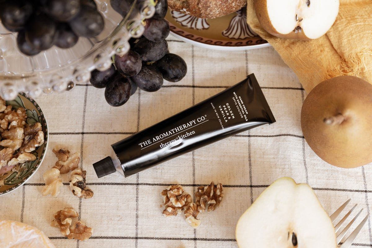 Hand cream tube on a check cloth beside a halved pear, walnut pieces and a silver fork