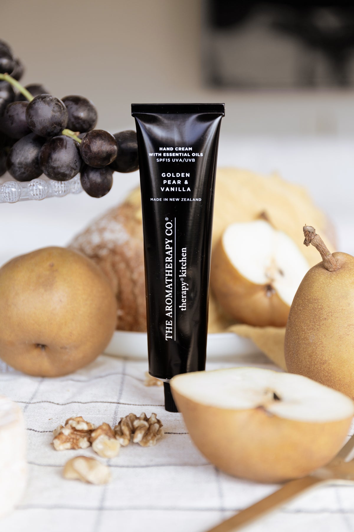 Golden Pear & Vanilla tube upright in a table setting with halved pears, walnuts and black grapes behind