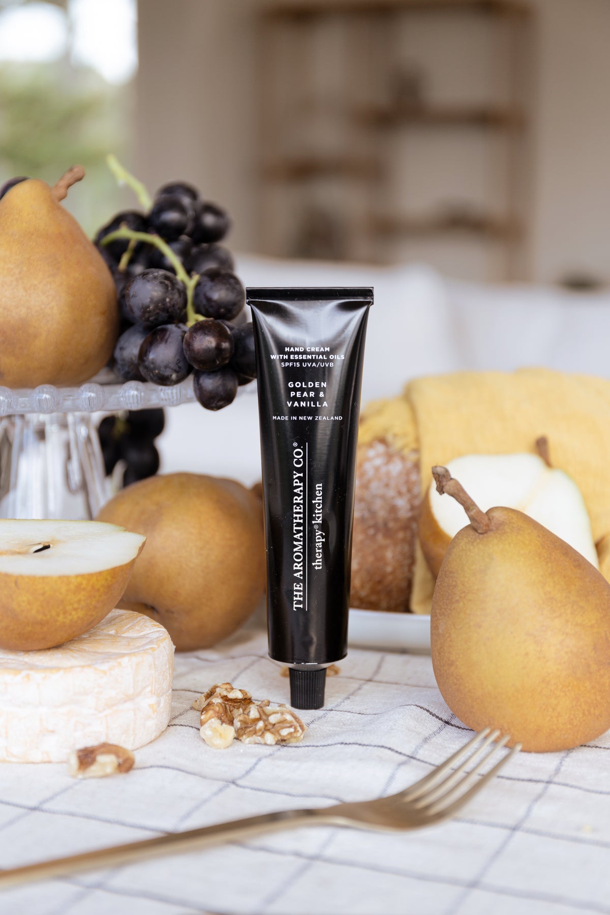 Golden Pear & Vanilla tube standing among pears, grapes and walnuts with a fork in front