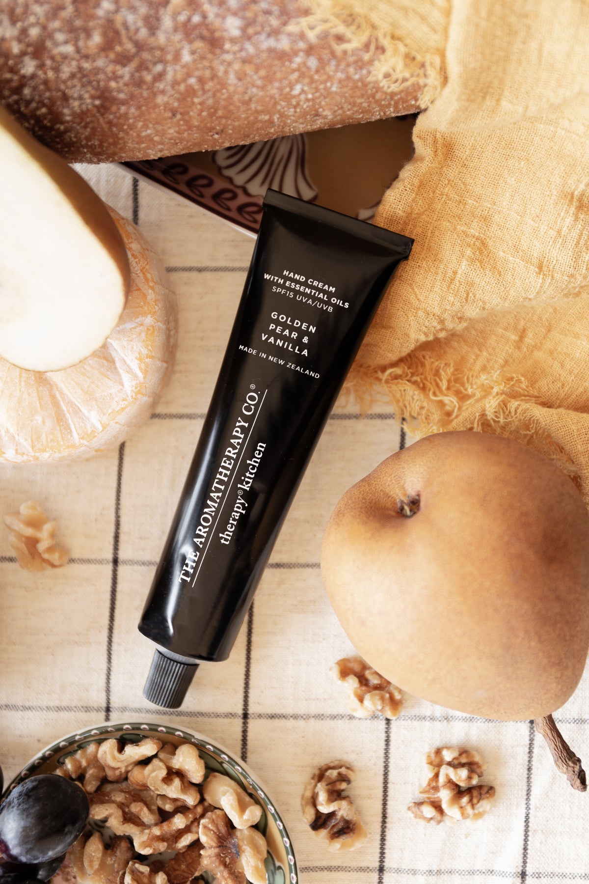 Tight crop of the Golden Pear & Vanilla tube diagonal on a check cloth with a whole pear and walnuts