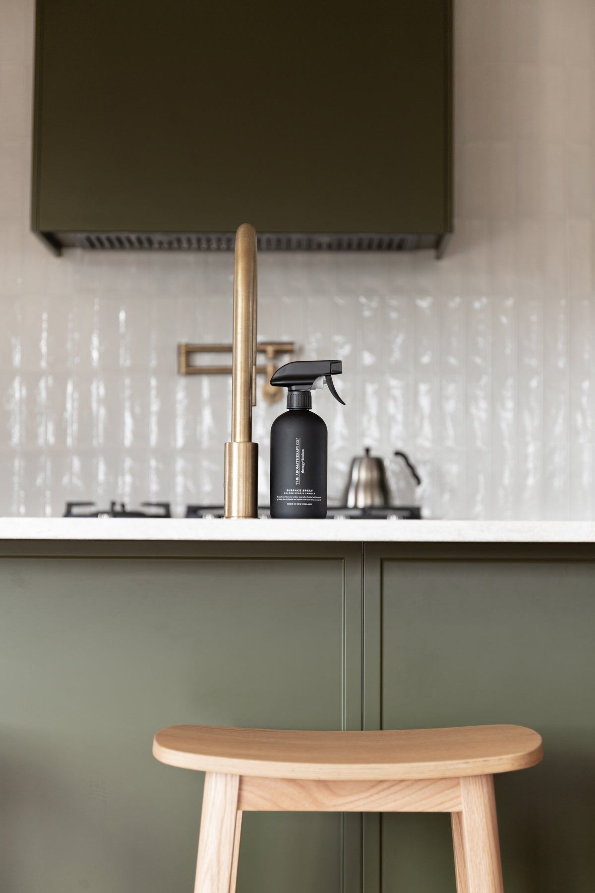 Black surface spray by a brass tap against a white fluted splashback, with a timber stool below