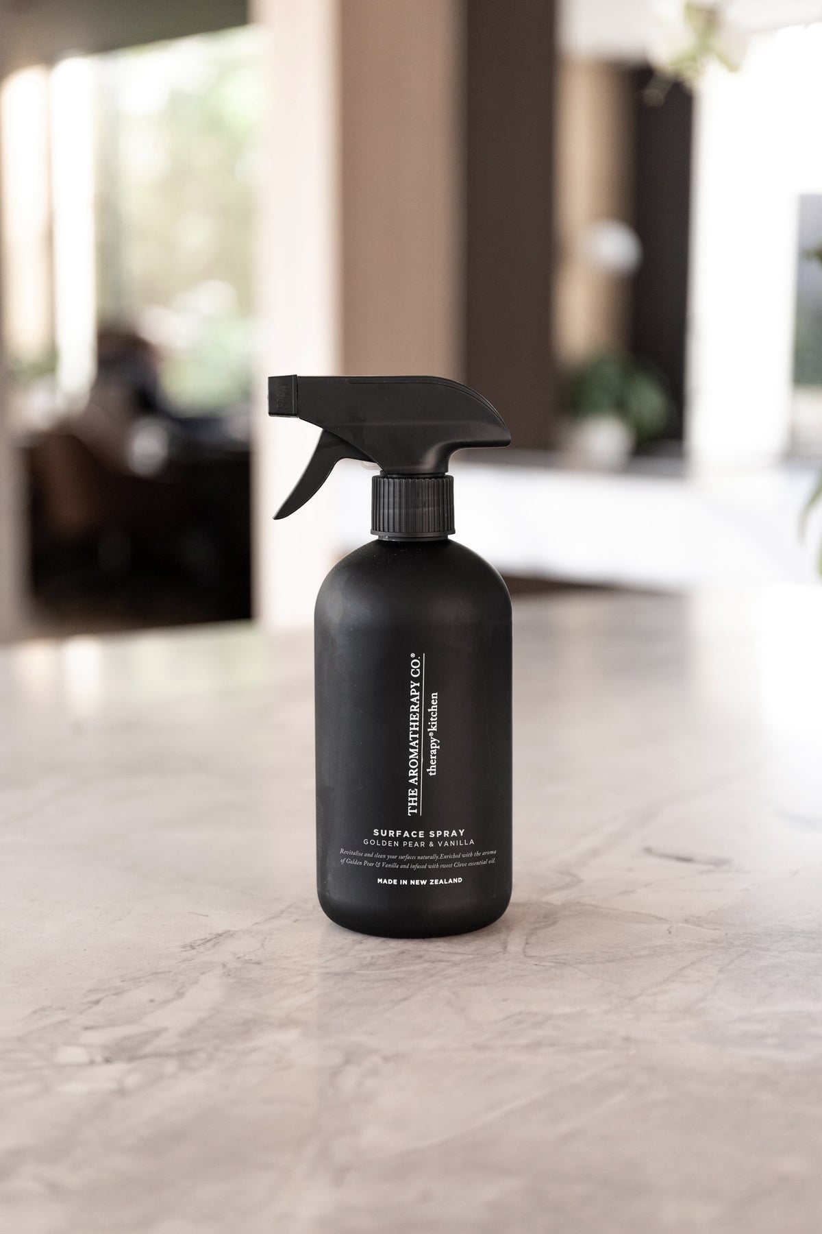 Black surface spray bottle on a marble benchtop in a blurred open plan living space