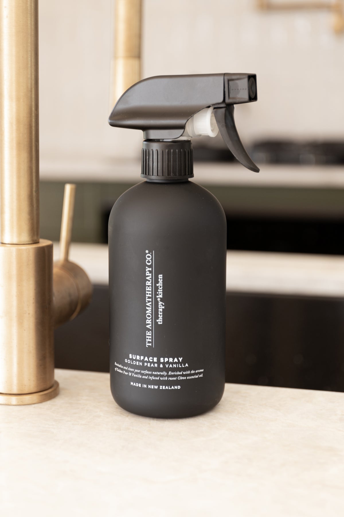 Close view of the black Golden Pear and Vanilla surface spray label beside a brass tap