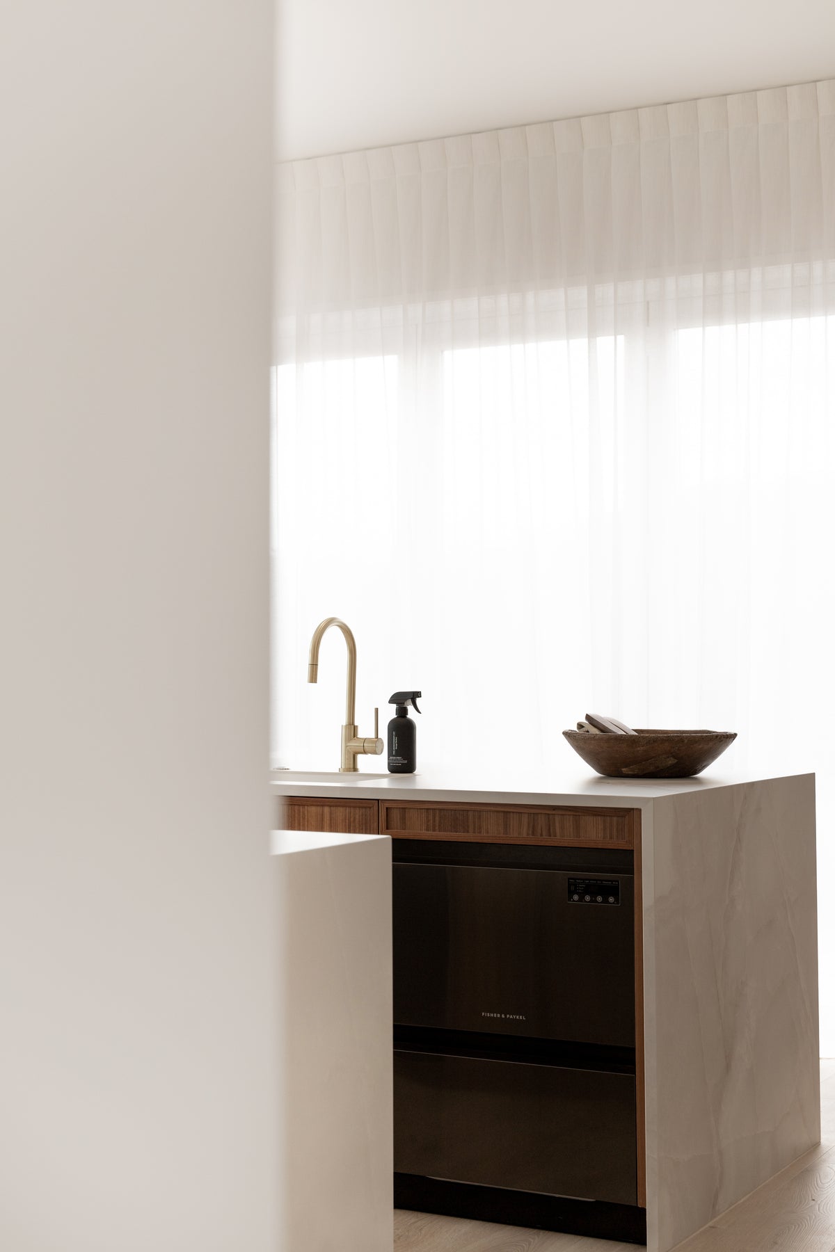 Wide view of a pale kitchen bench with the black surface spray, a brass tap and a wooden bowl