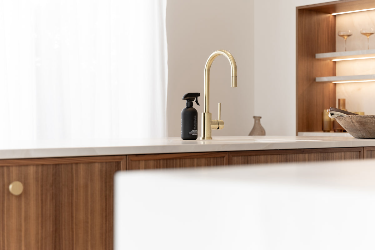 Black surface spray on a kitchen bench with brass tap, timber joinery and lit glass shelving