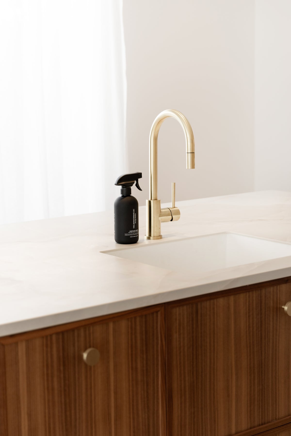 Black surface spray beside a brass tap at a white sink with timber cupboards below