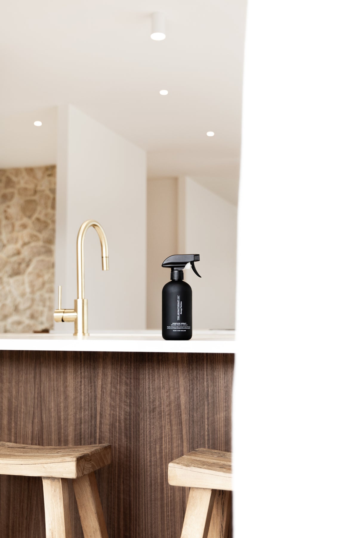 Black surface spray on a kitchen island with a brass tap, stone wall and timber stools