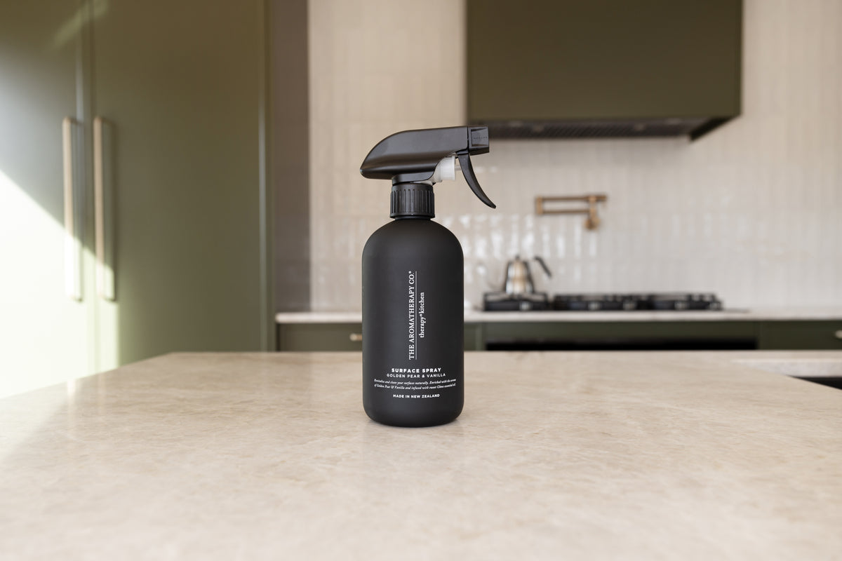 Black surface spray on a stone island in an olive green kitchen with a brass kettle behind