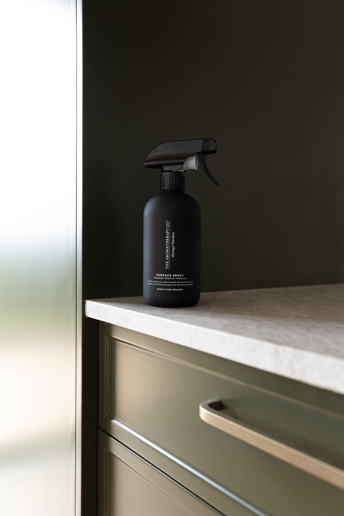 Black surface spray on a stone benchtop above olive green drawers with a brass handle