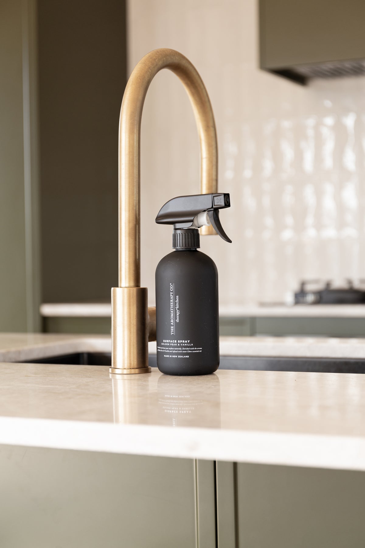 Black surface spray beside a brass tap in an olive green kitchen with white tiles