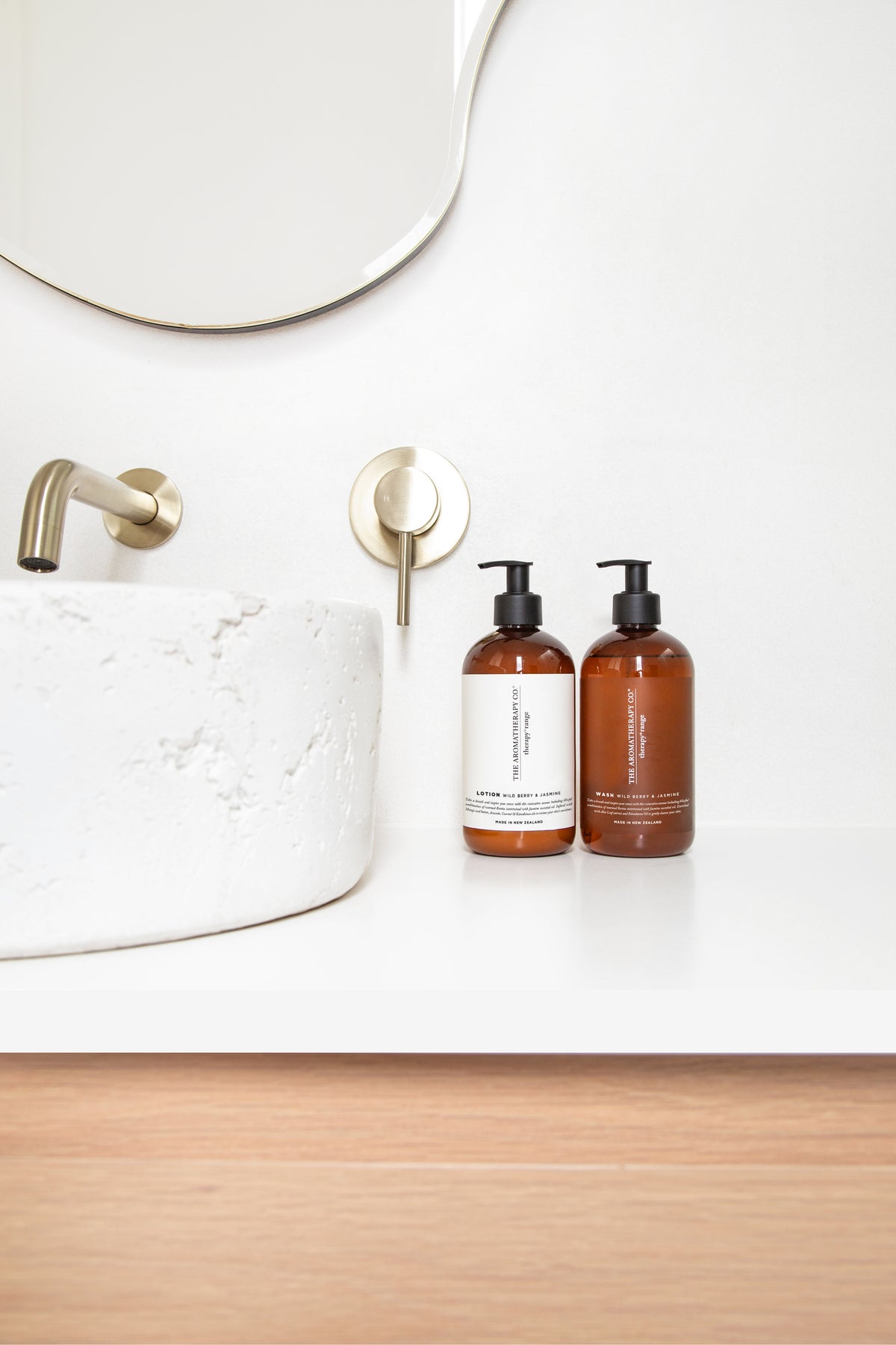 Amber pump bottles beside a stone vessel basin on a white vanity, brushed tapware and a round mirror above