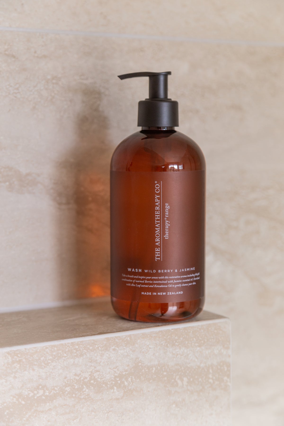 A single amber Therapy pump bottle standing on a travertine ledge, warm light across the stone