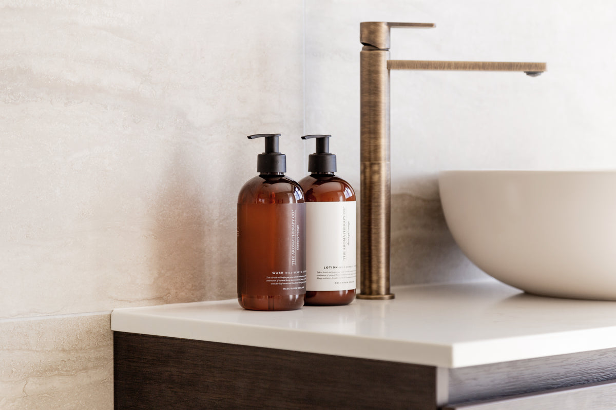 Amber pump bottles on a dark timber vanity beside a stone basin and a tall brushed tap