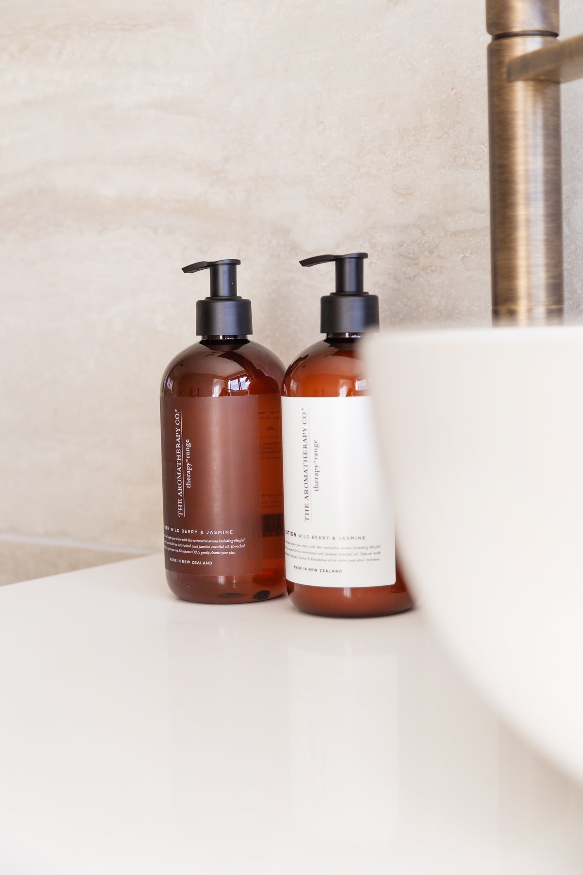 Two amber Therapy pump bottles beside a white basin, one label facing forward, brushed tap behind