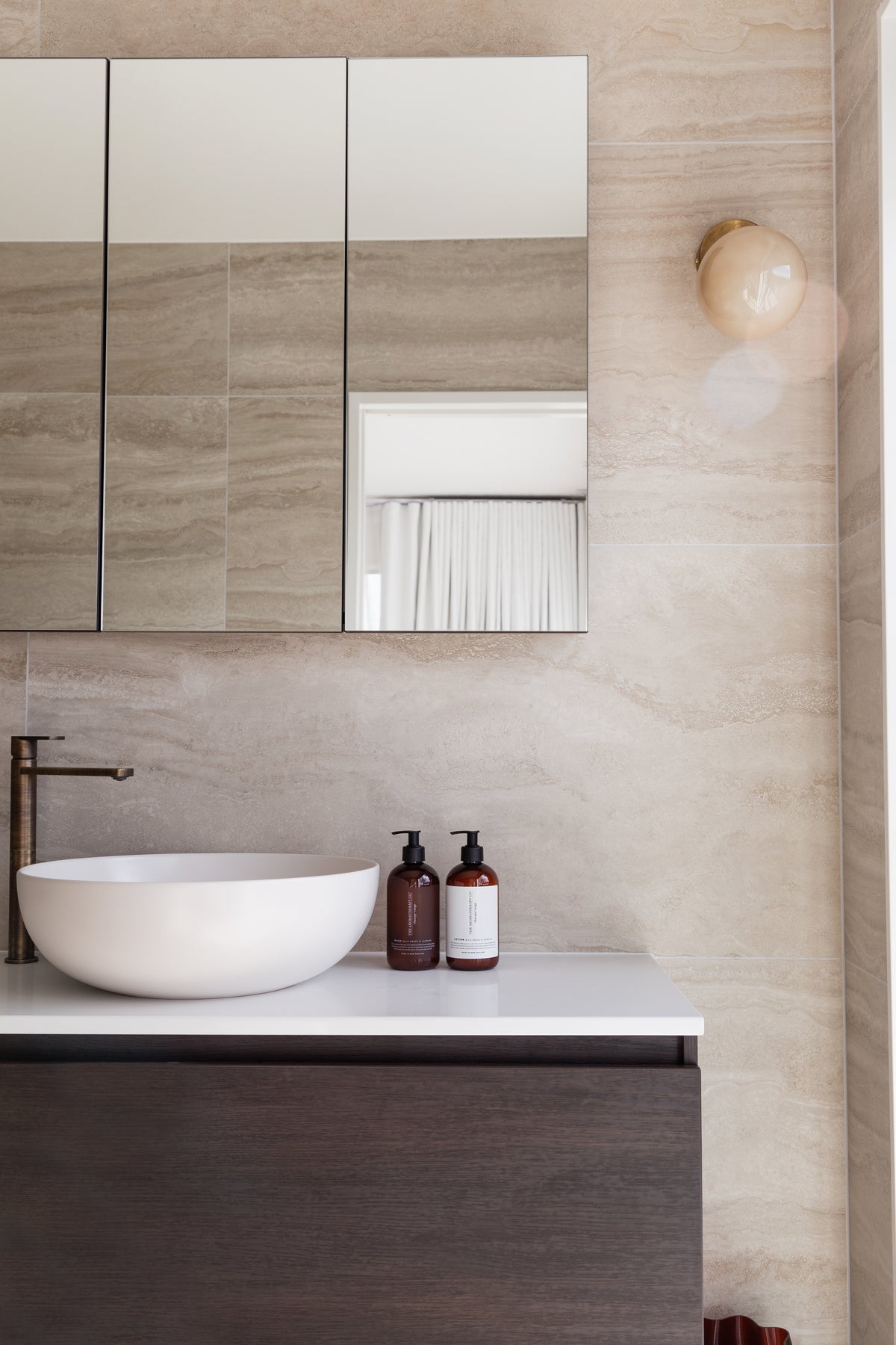 Bathroom with a mirrored cabinet and dark timber vanity, amber pump bottles beside the basin