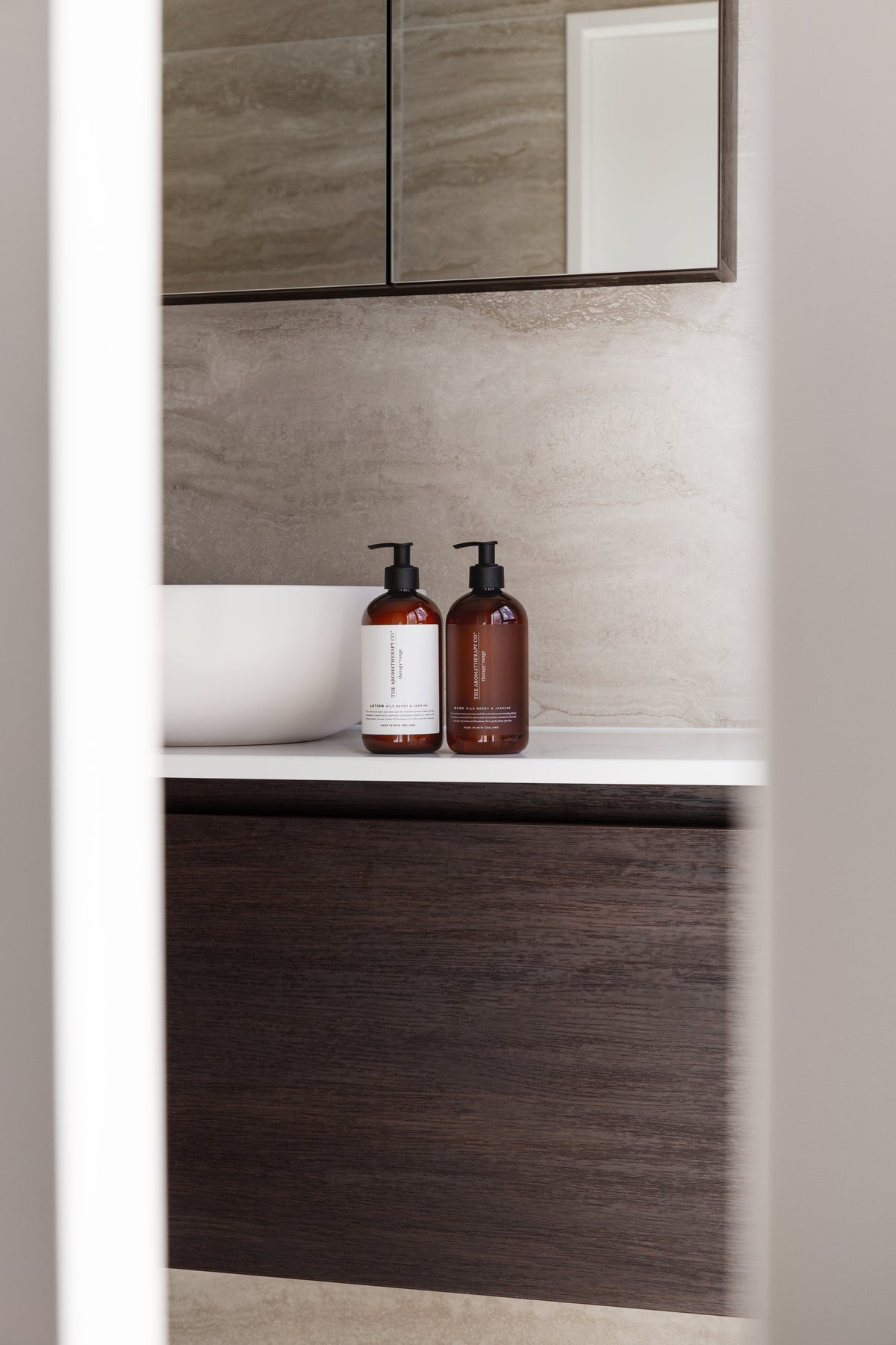 Bathroom niche with a white basin and two amber pump bottles, mirrored cabinet above