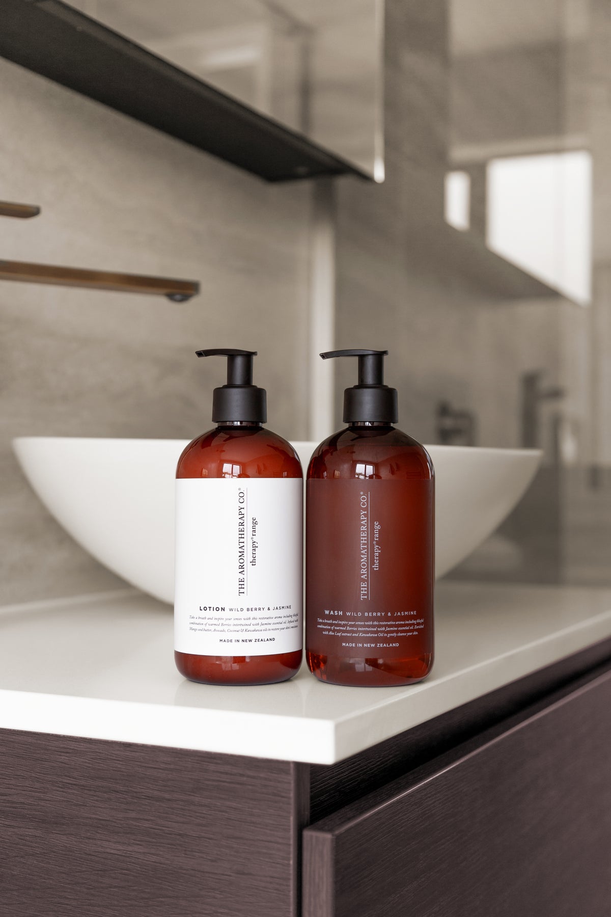 Two amber Therapy pump bottles on a white vanity beside a round basin, dark timber beneath