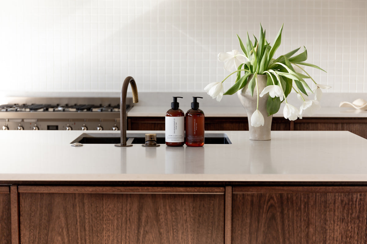 Dark timber kitchen island with a vase of white tulips, amber pump bottles beside the tap