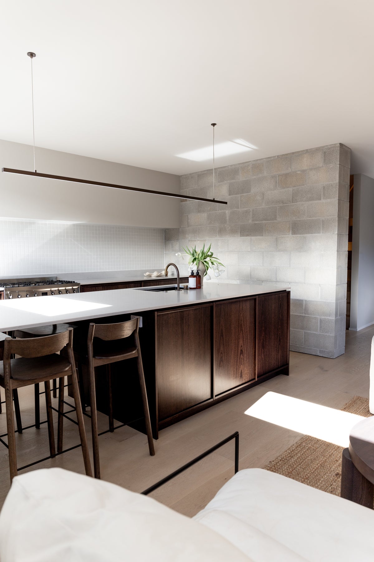 Open kitchen with a dark timber island and bar stools, amber pump bottles small on the bench
