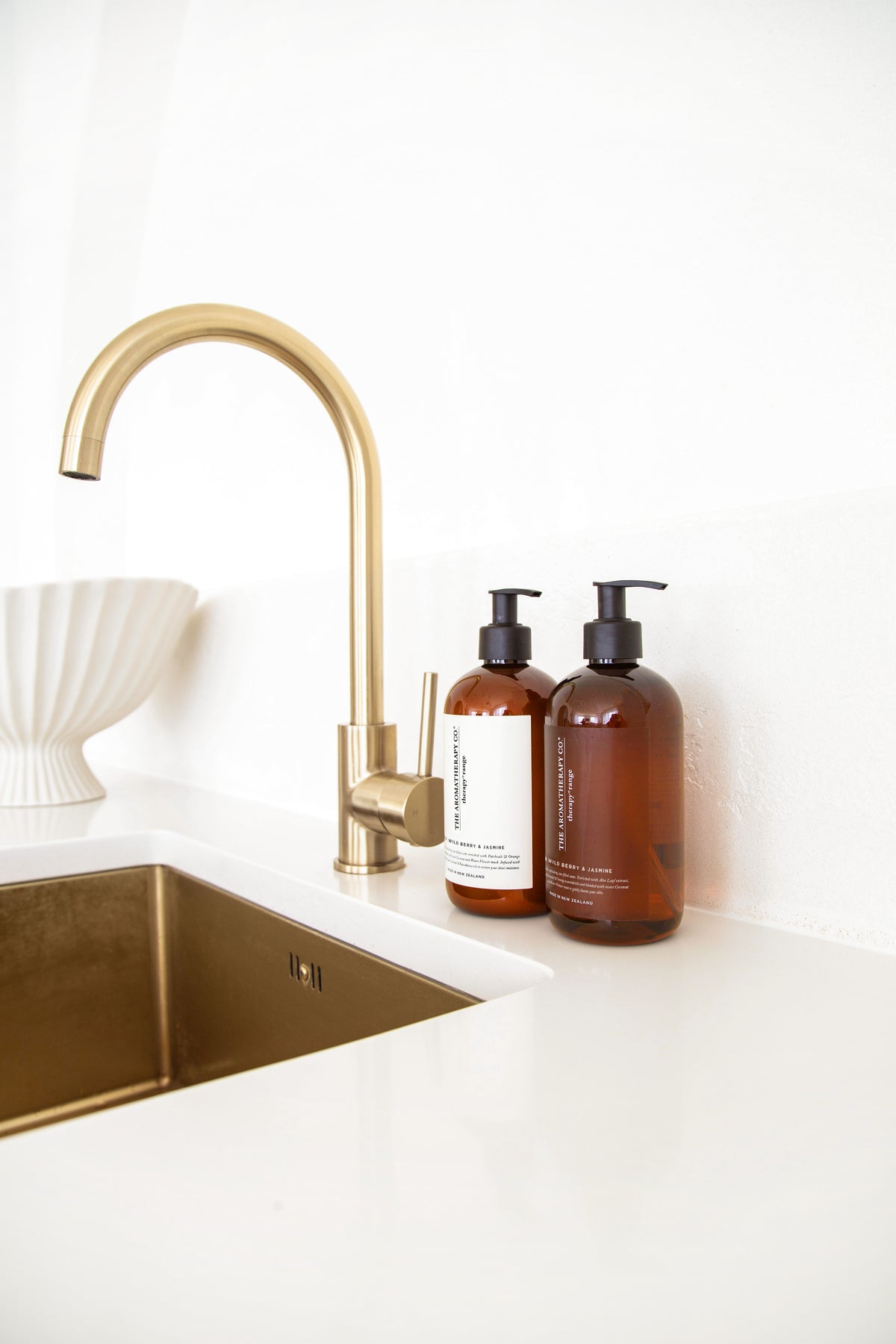 Gold tapware over a gold sink, two amber Therapy pump bottles on the white benchtop