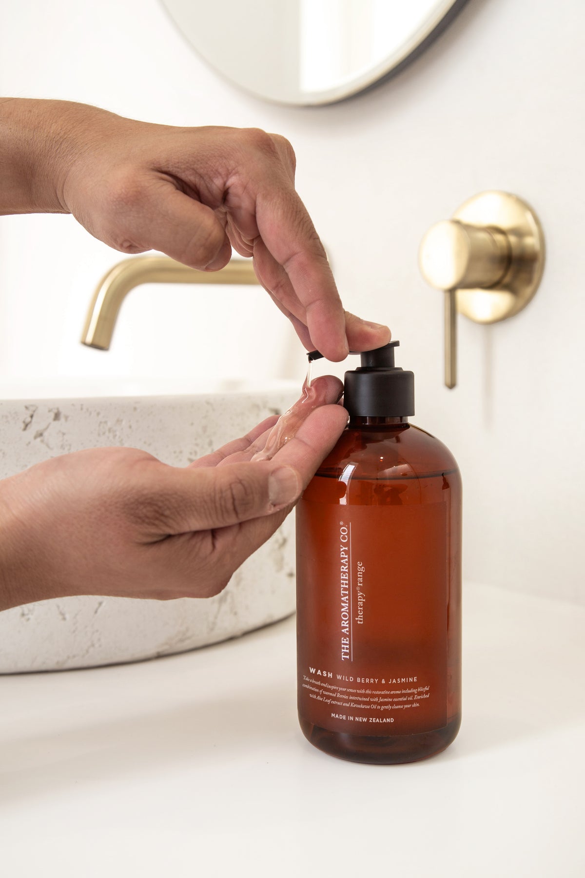 A hand pressing the pump on an amber Therapy bottle at a stone basin