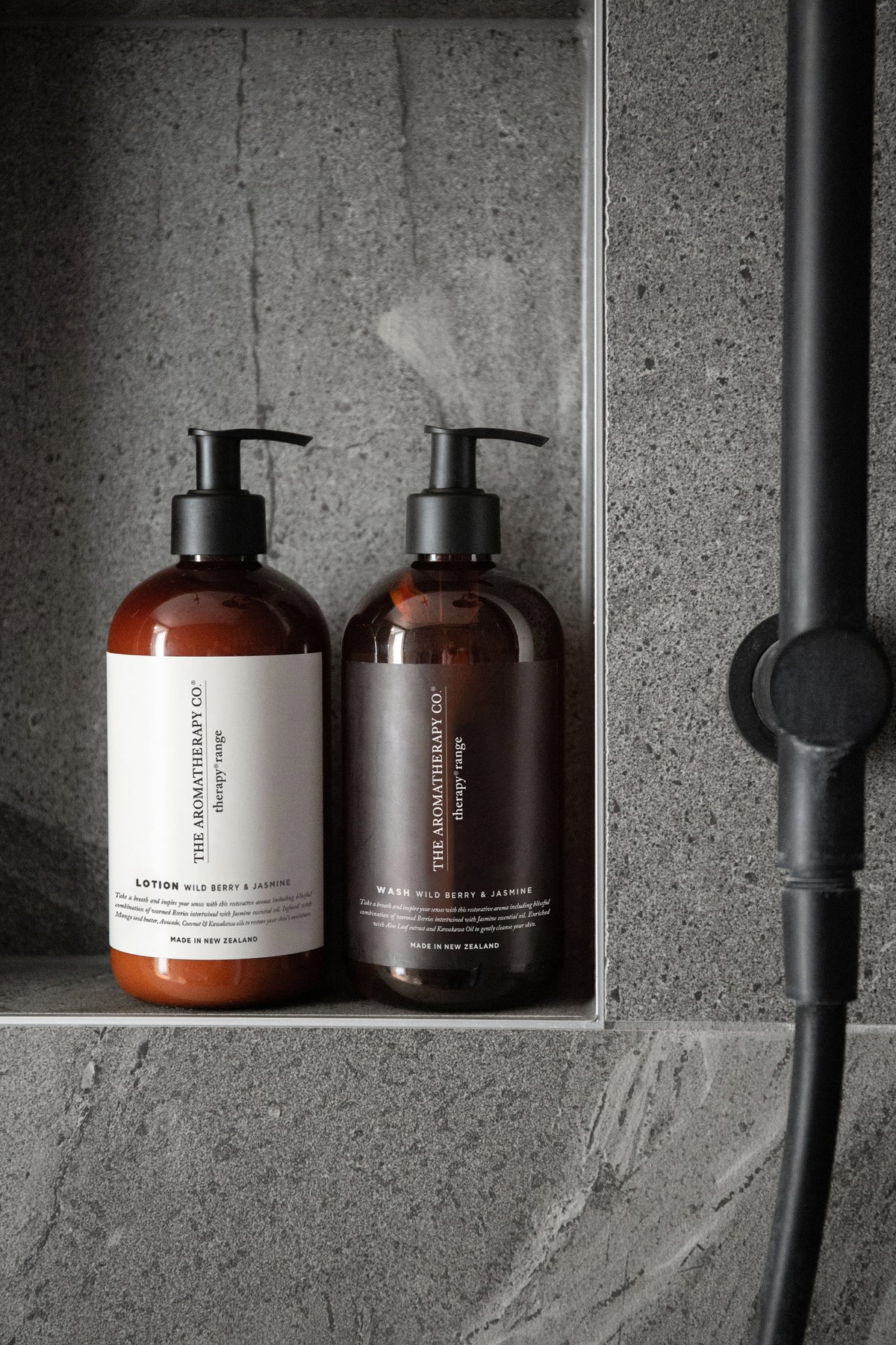 Two amber pump bottles in a grey stone shower niche beside the shower rail