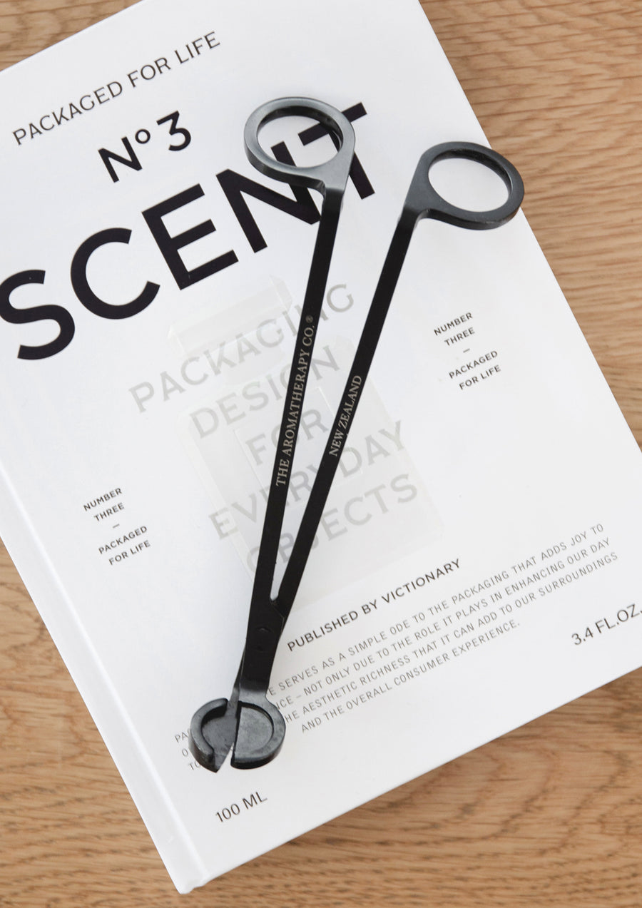 Black wick trimmer laid across a white design book on light oak