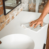 A man cleaning a bathroom counter with Good Change's ECO CLOTH - LARGE (2-PACK).