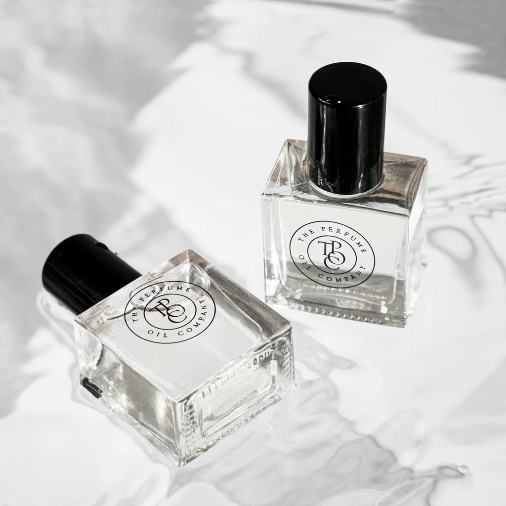 Two square glass perfume oil bottles lying on white marble