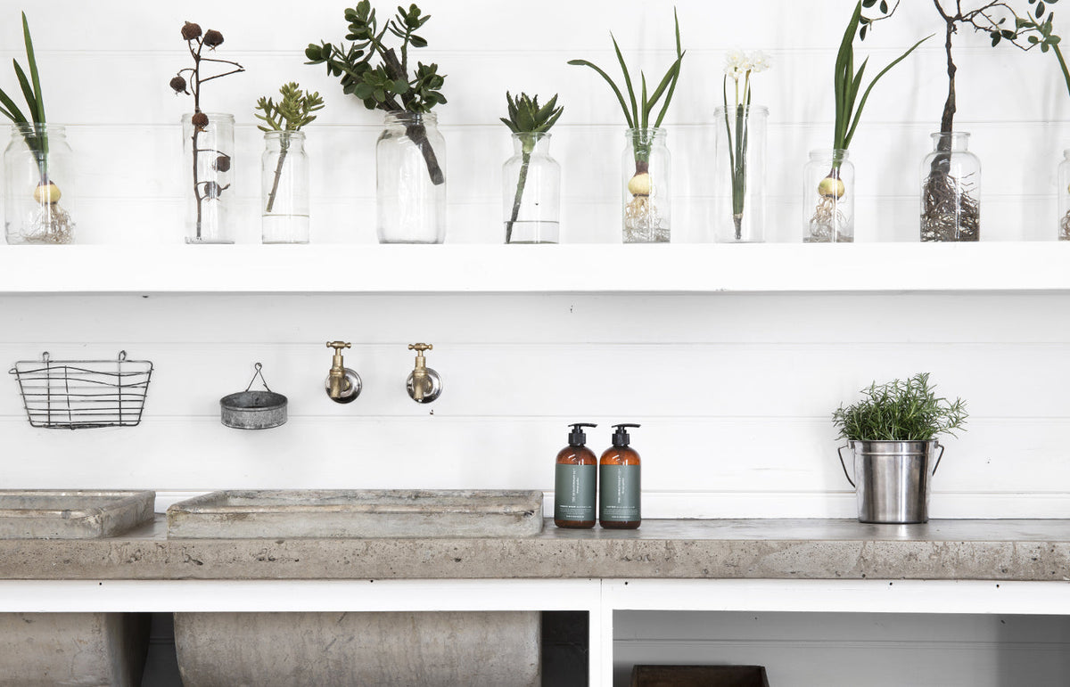 Wide view of a potting bench with brass taps, two Therapy Garden bottles and a potted herb