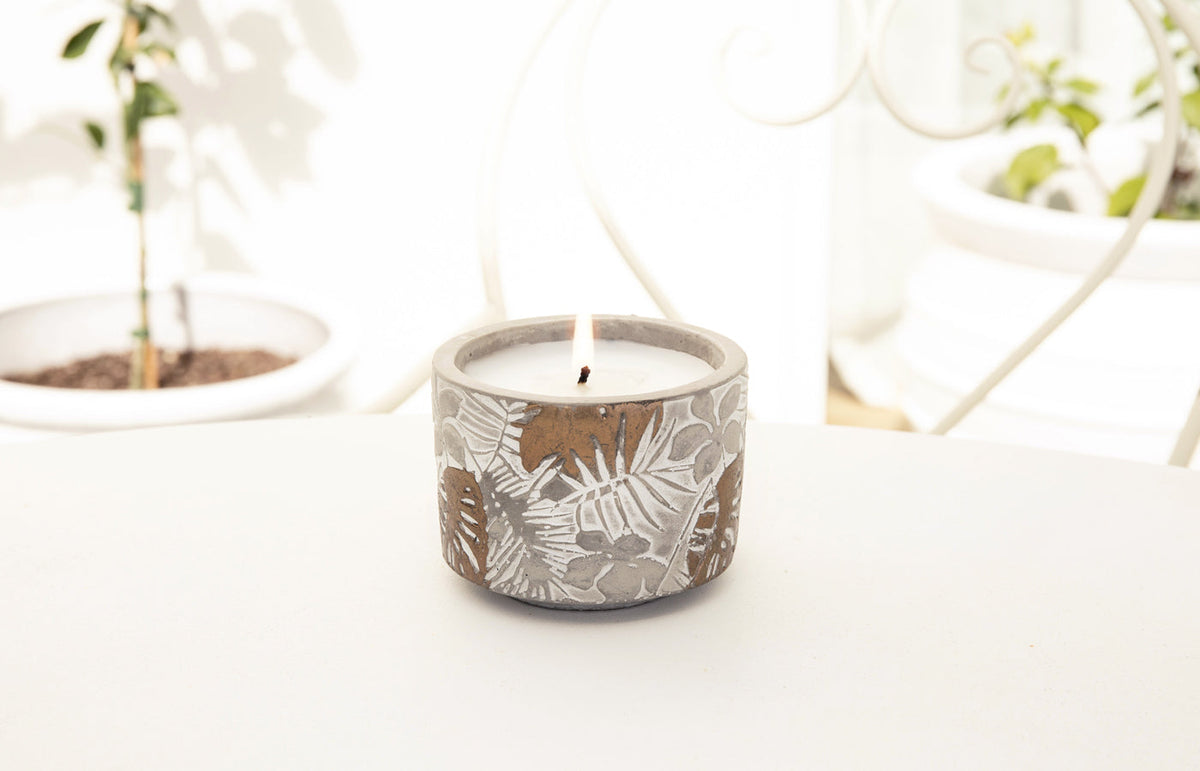 Lit outdoor candle on a white outdoor table with potted seedlings behind, landscape view
